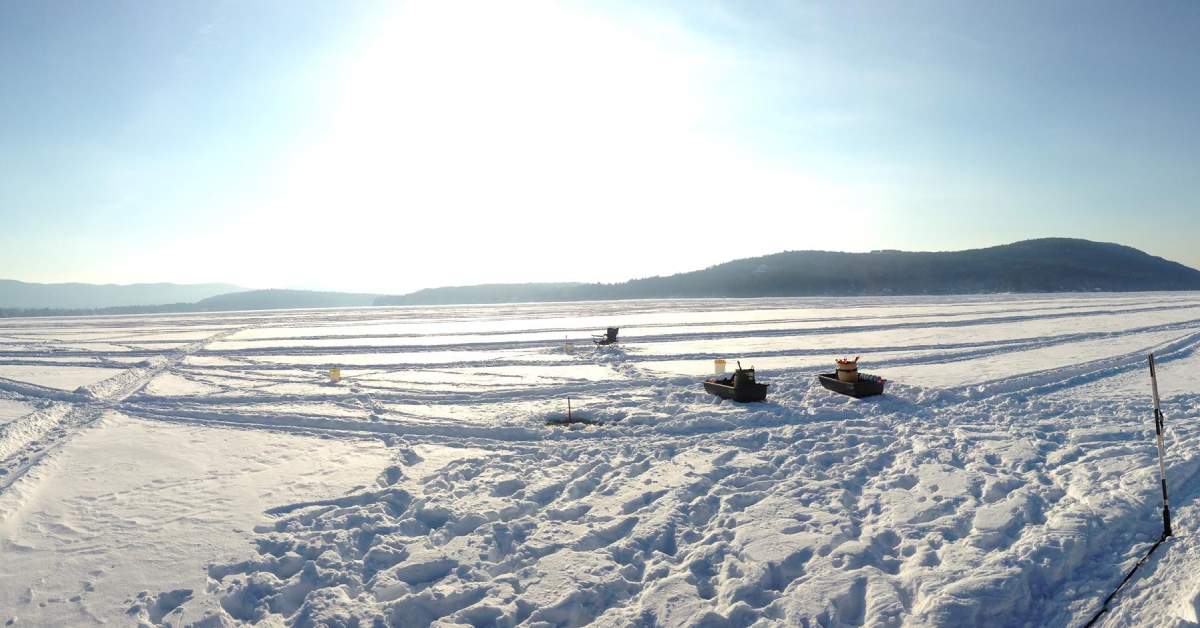 two sleds by ice fishing holes on a lake covered in snow