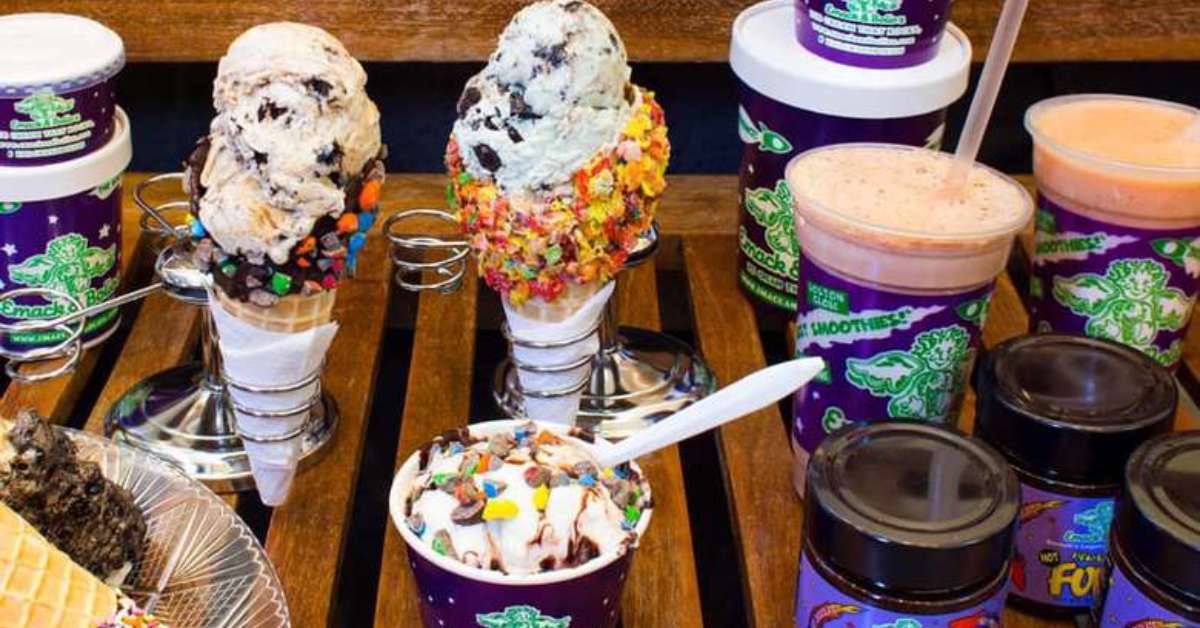 a variety of sweets on a bench, including ice cream, pastries, drinks, and more. 