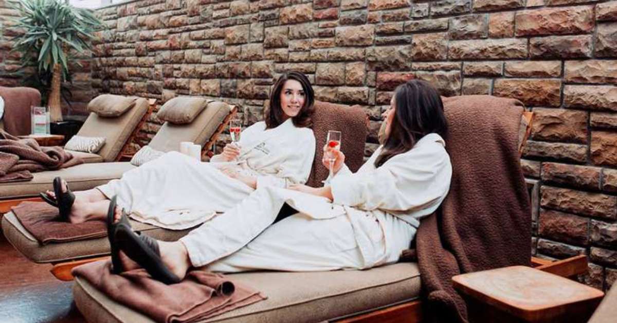 two women chatting on lounges in a spa and sipping drinks