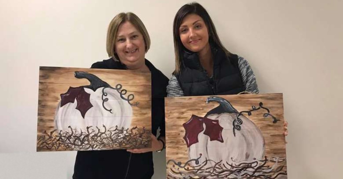 two friends holding pumpkin paintings