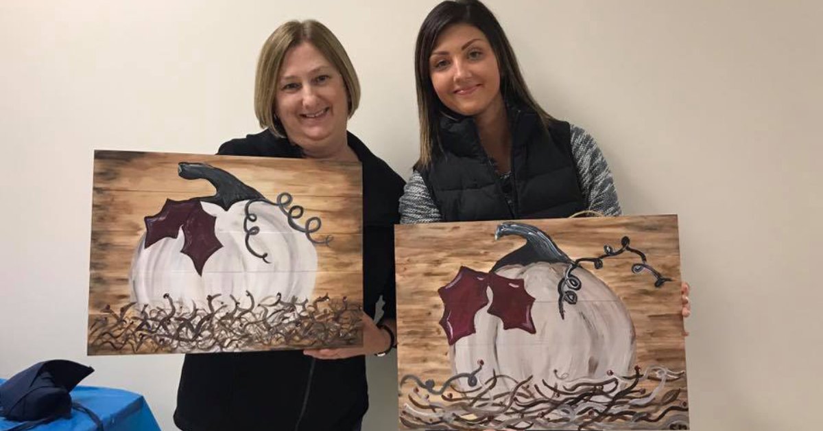 two women holding up paintings of white pumpkins