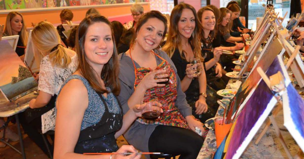women sitting and holding drinks at a paint and sip class