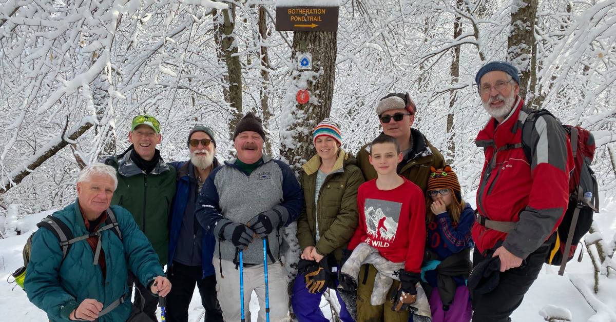 snowshoeing group poses by trail sign