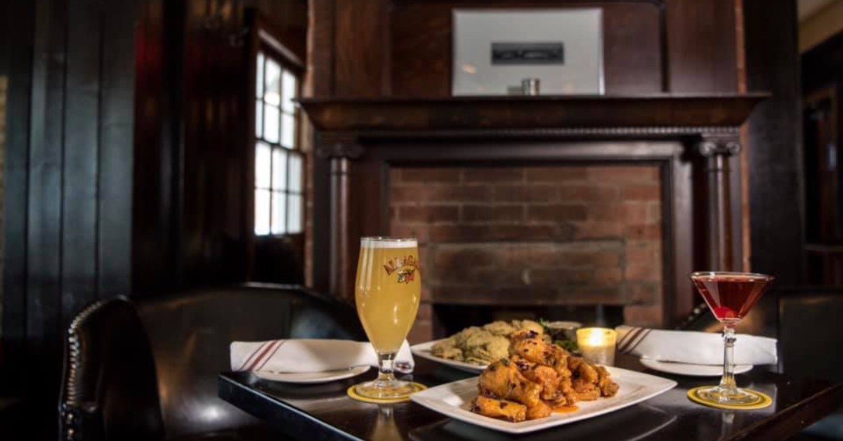 wings and a martini and beer on a table in front of a fireplace