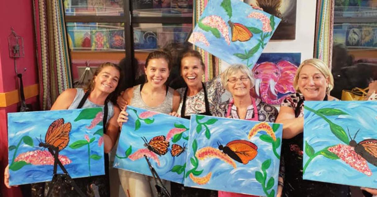 several women holding up their paint and sip paintings