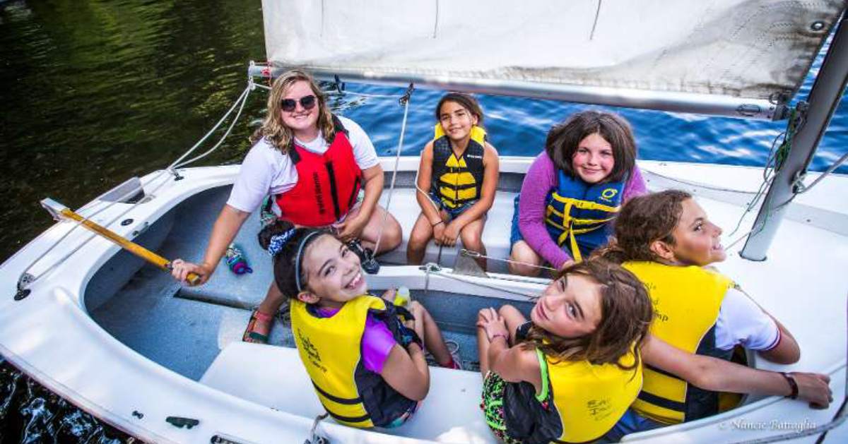 girls smiling in a sailboat with a counselor