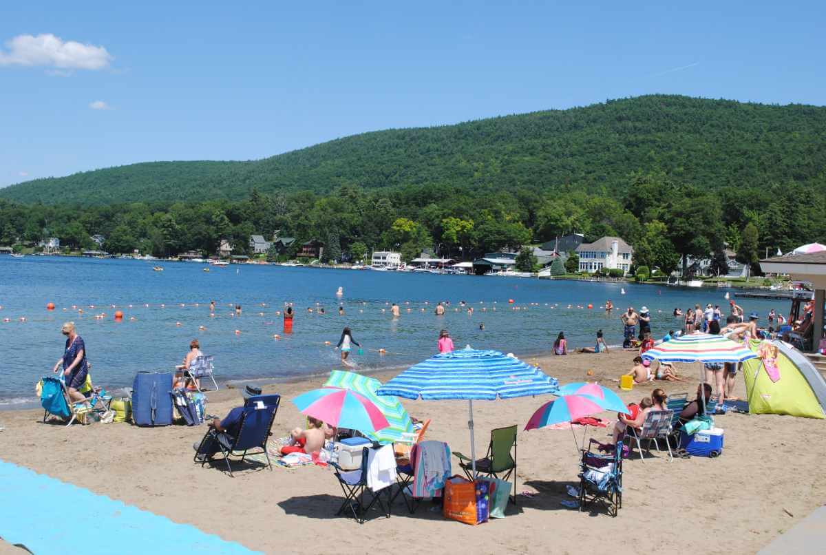 A crowd of people and colorful beach umbrellas at million dollar beach in lake george, ny on a warm, sunny day