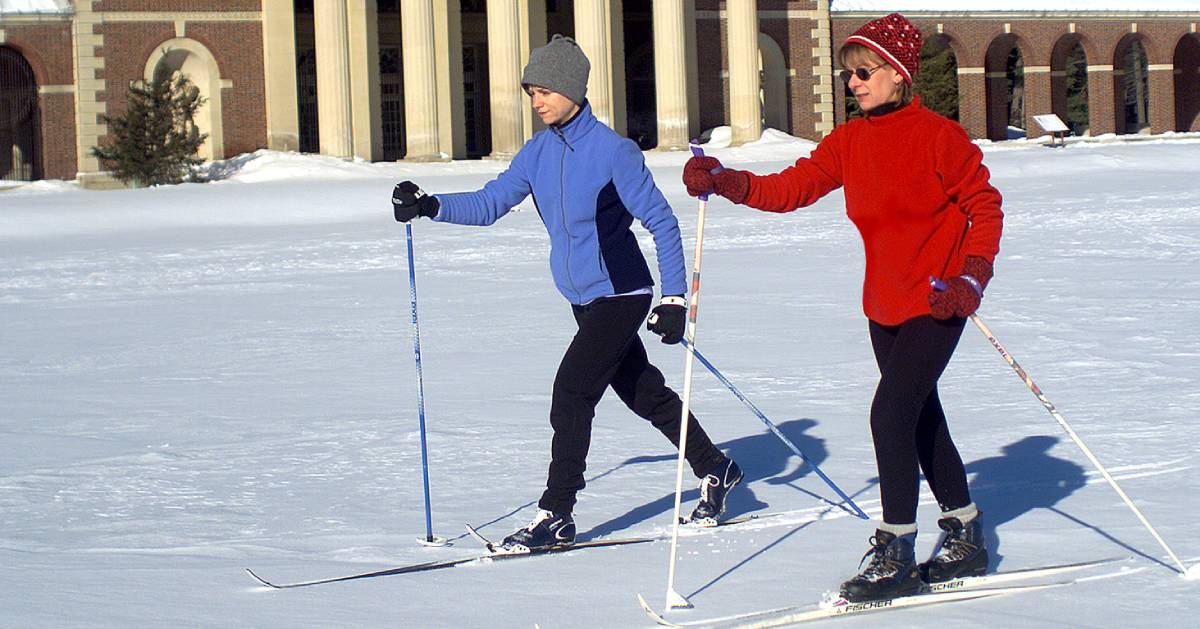 two people cross country skiing with building in background