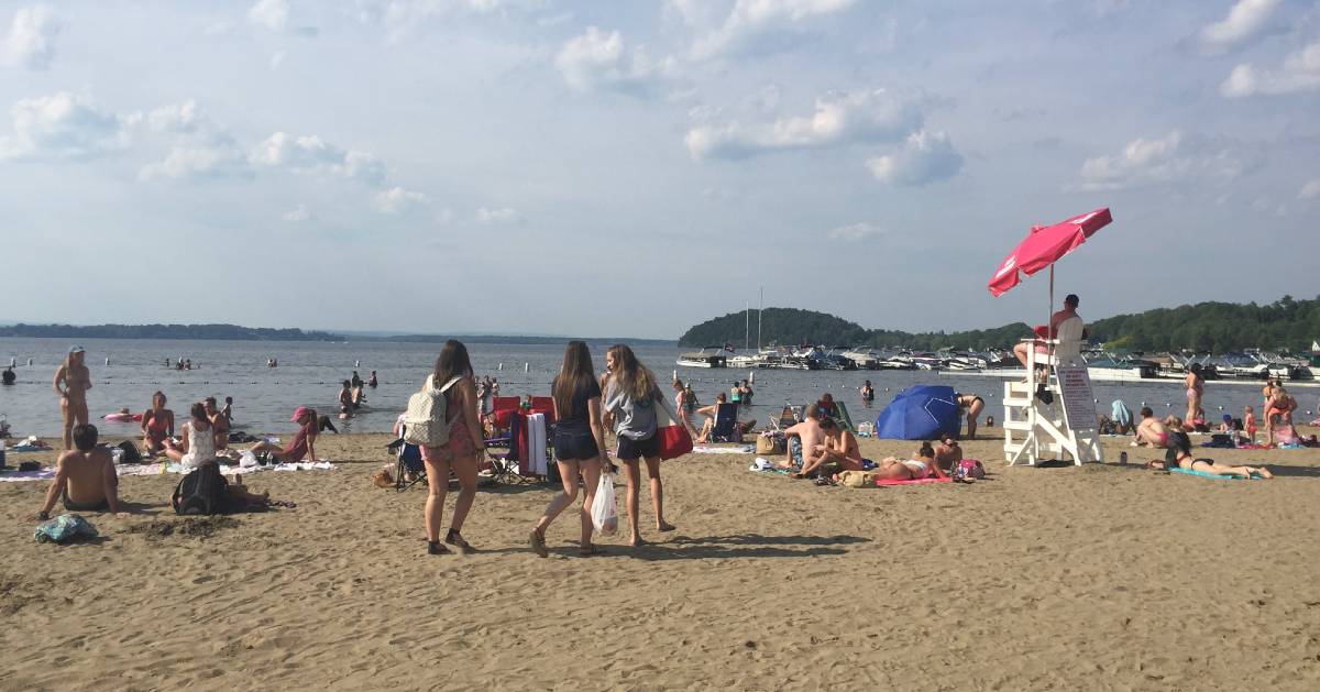 people walking on sandy beach by a lake