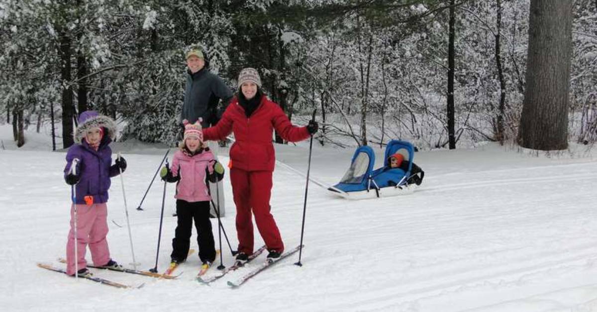 man, woman, and three kids cross country skiing together