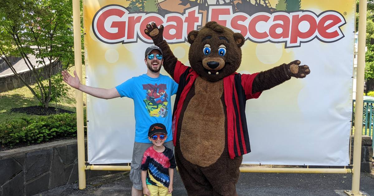 dad and son pose in front of Great Escape sign with costumed character