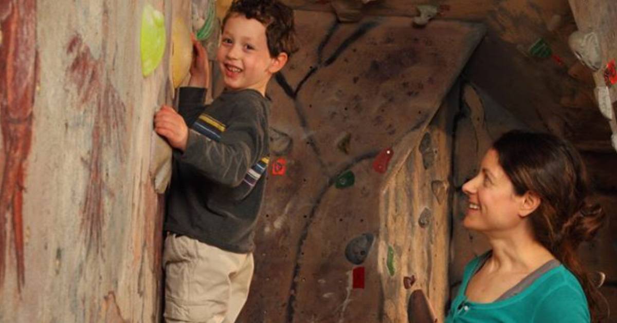 boy climbing rock wall with woman nearby to help