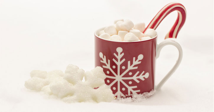 red coffe cup with white snowflake on it holding cocoa with marshmallows and a candy cane