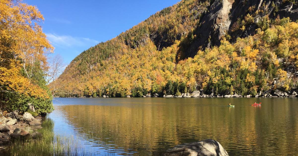 faraway view of two kayakers by a mountain in the fall