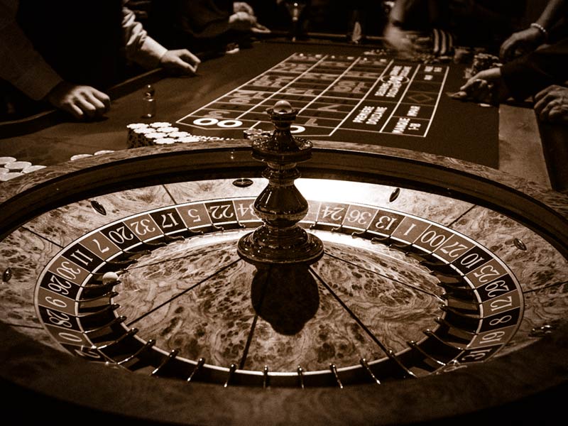 Close up of a roulette table with gamblers placing bets in the background