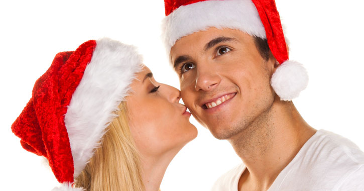 woman kissing man on the cheek; both wearing santa hats
