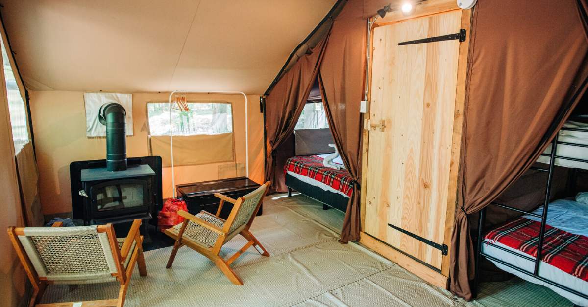 inside of a glamping tent with beds, seating area, and stove