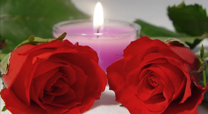 two red roses in front of a small, pink, lit candle