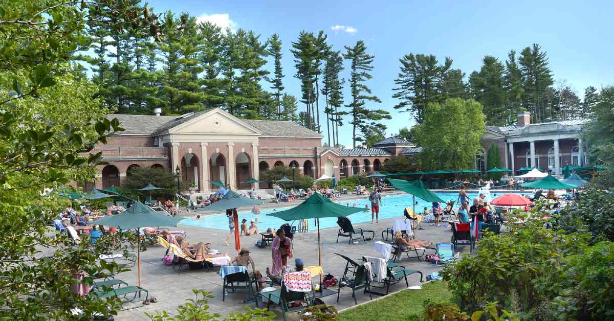 people relaxing around a large outdoor swimming pool near brick buildings