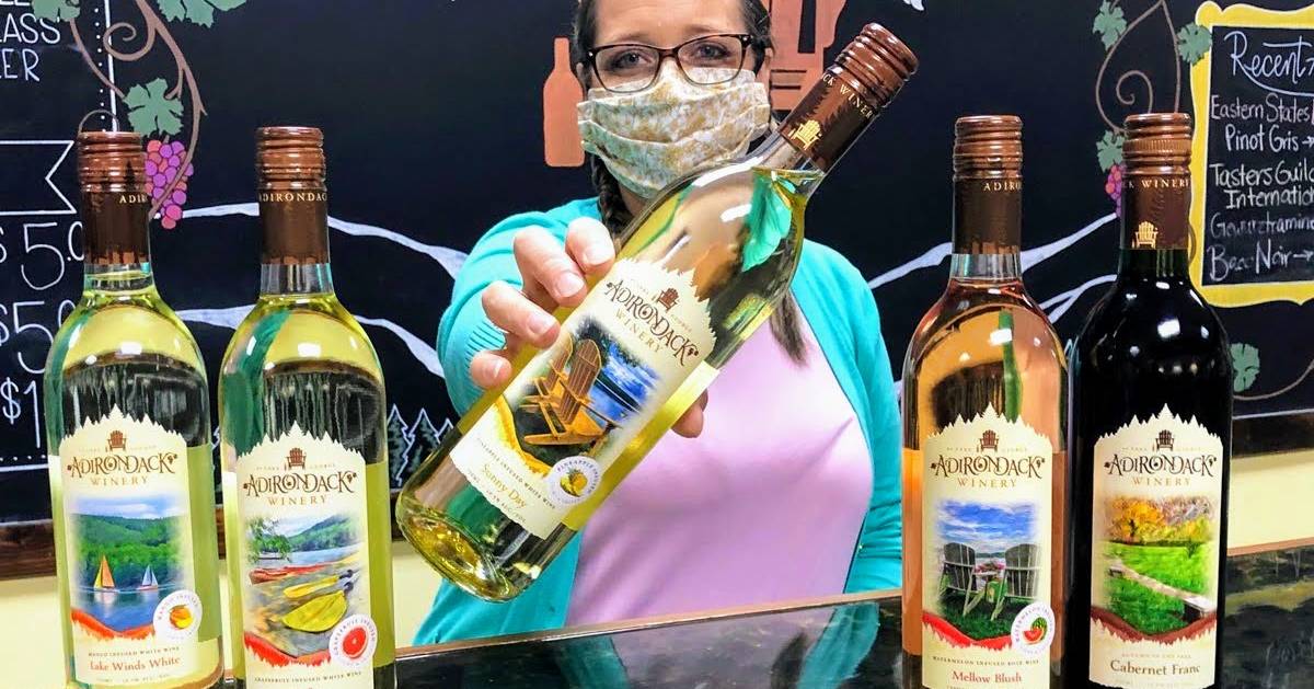 masked woman holding out Adirondack Winery wine bottle