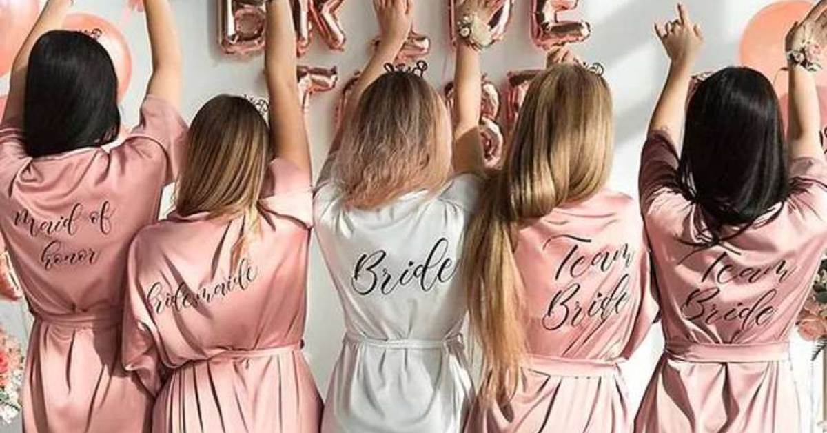 four bridesmaids and one bride with designated robes lifting hands with their backs to the camera