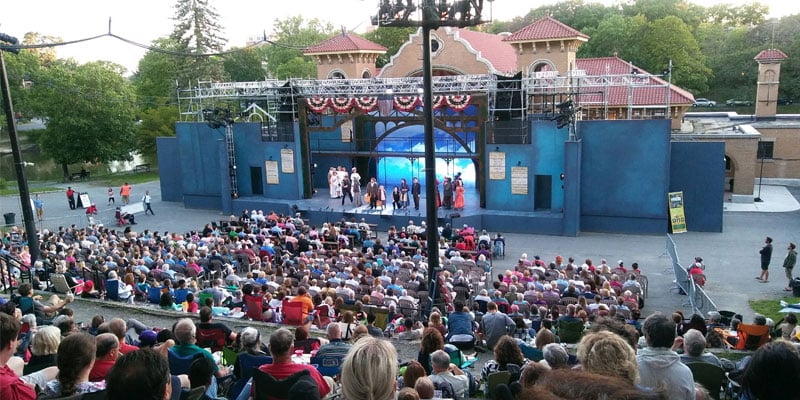 a production going on at a lake house amphitheater with a large crowd