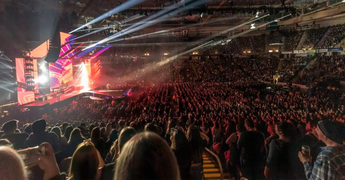 a huge group of people at an indoor concert with bright lights