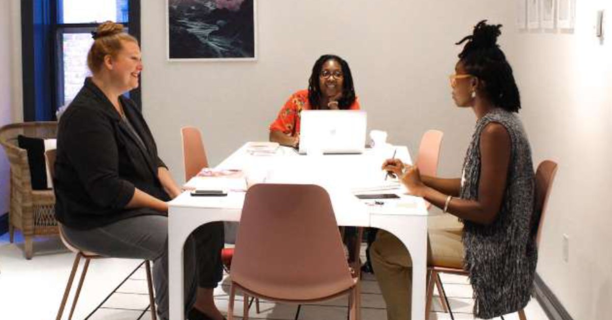 three women talking at a work table with ipads and computers