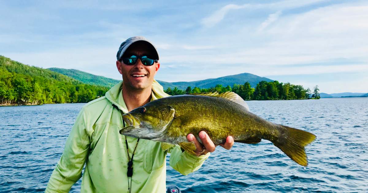 man in a green shirt holding up a fish on a boat