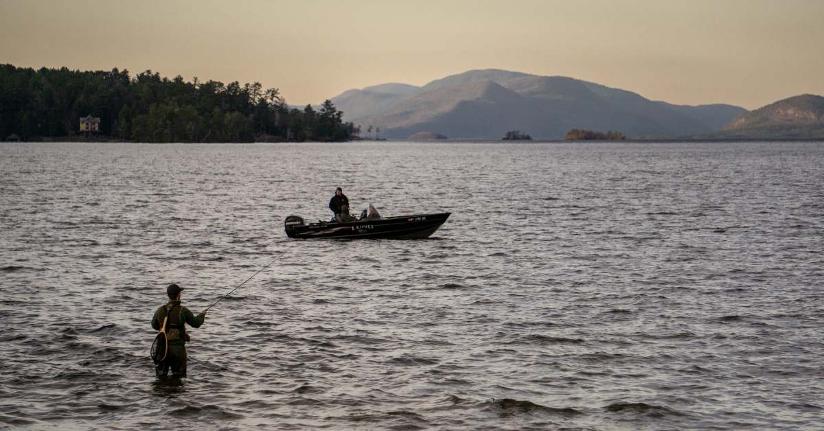 silhouette two men fishing, one in the water one, one on a boat