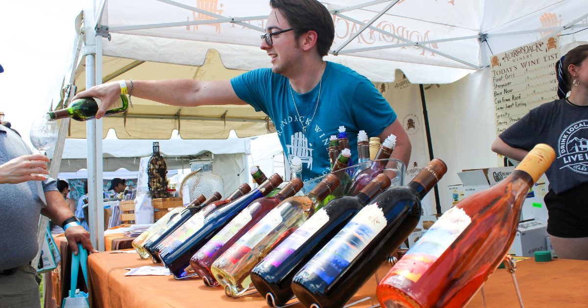 man with glasses pours wine at vendor tent