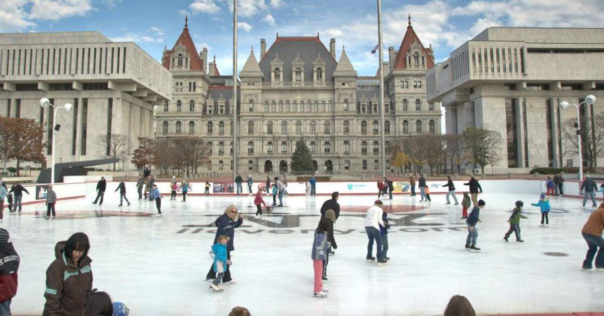people ice skating outdoors near city buildings