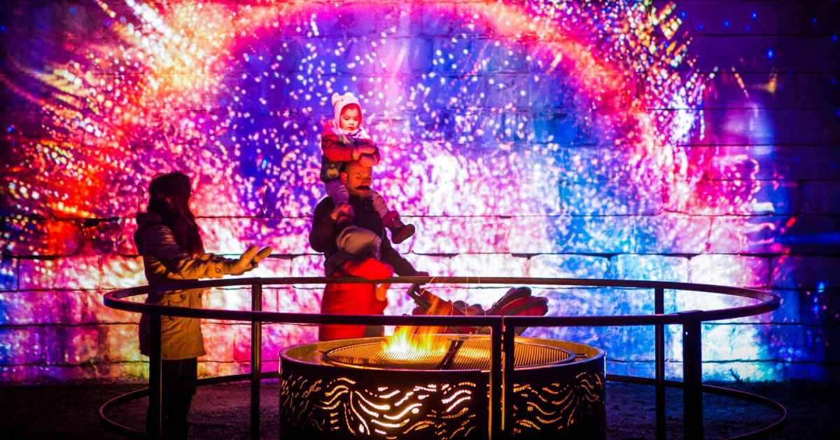 man, woman, and child standing near fire pit with colorful lights in the background