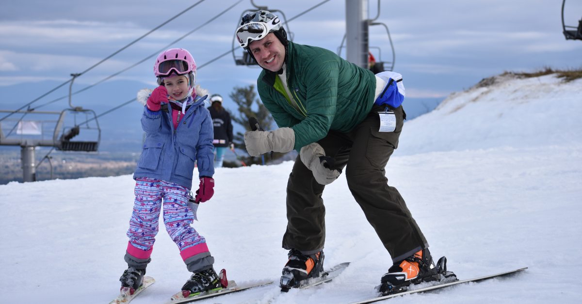 dad and daughter on skis giving a thumbs up