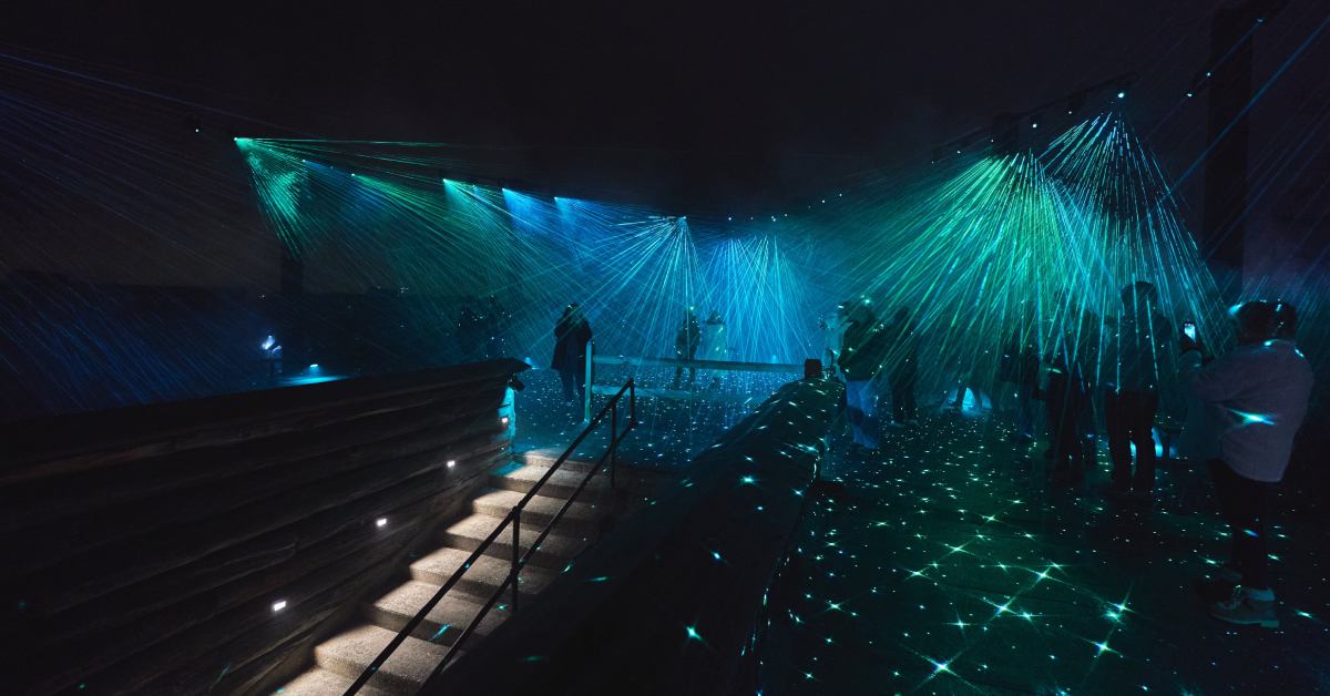large view of people standing under a green blue light display at night