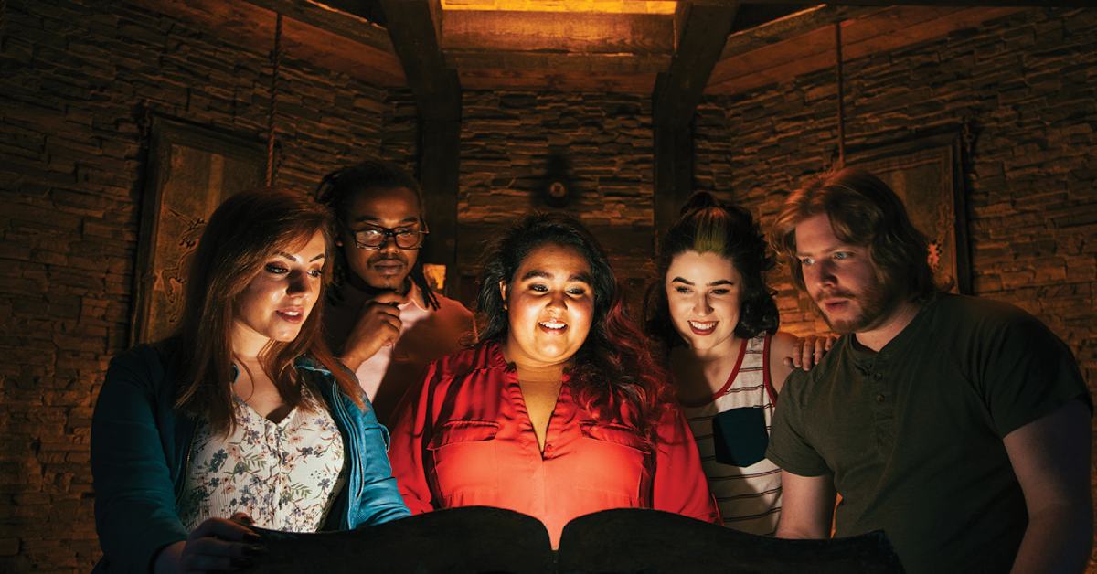 five people standing around a book in a fake tomb room