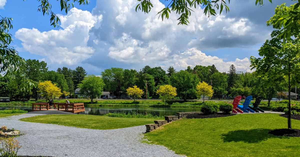 gravel path leading to adirondack chairs and a pond overlook on a sunny day