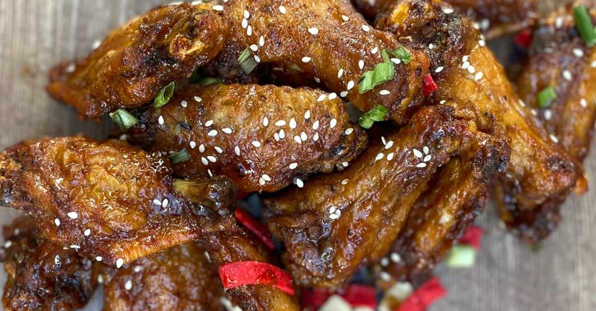 cooked chicken wings with sauce, sesame seeds, and green onions on them