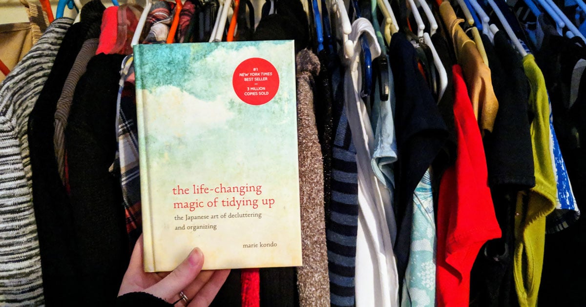 Marie Kondo book held in front of clothes in closet