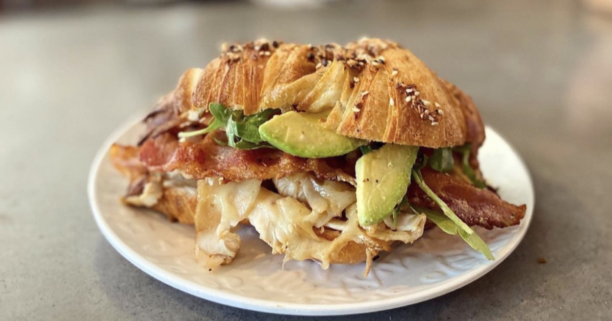 croissant with turkey, bacon, avocado, and arugula on it