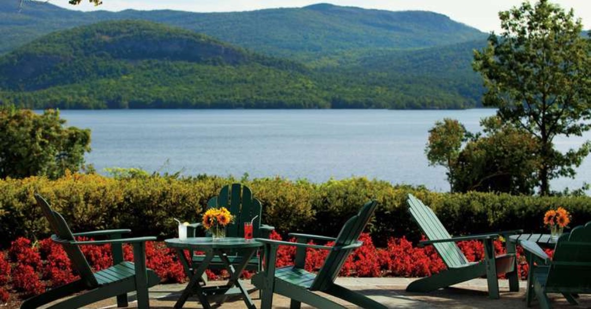 adirondack chairs and tables on a patio overlooking a lake with mountains in the background