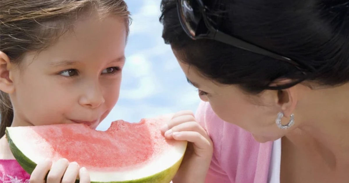 a girl eating watermelon and looking at her mother