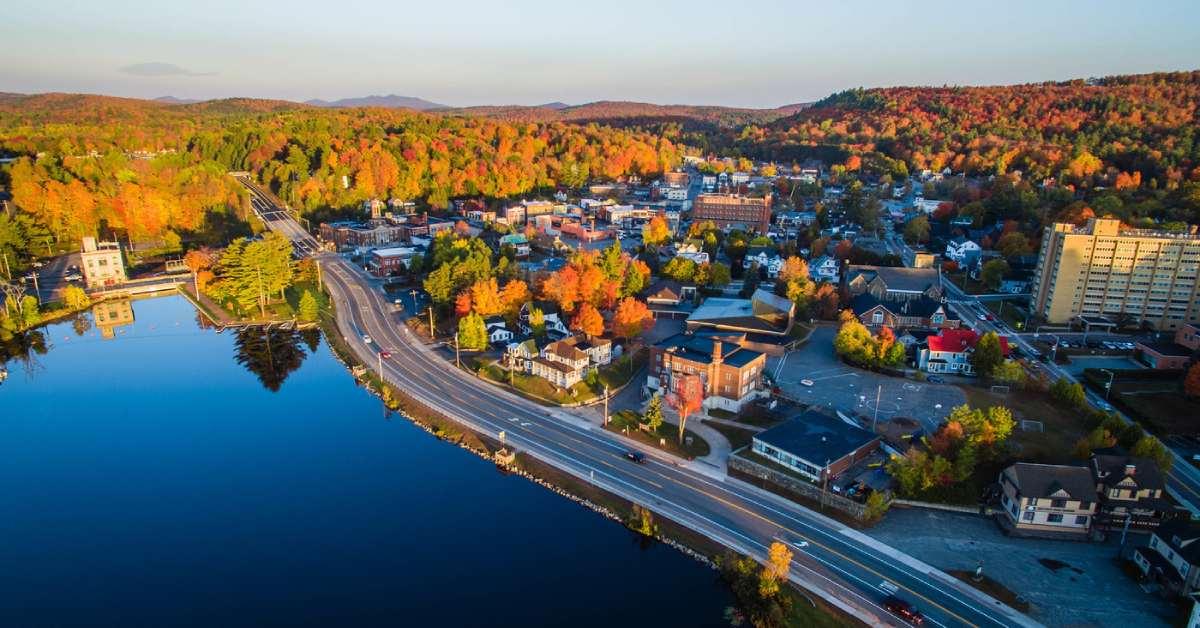 aerial view of a town with a lake to the left and colorful trees in the background