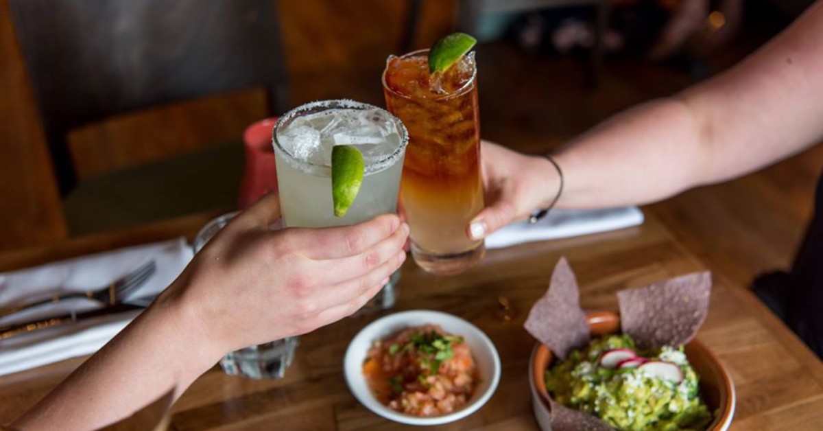 two people raising glasses above table with salsa, chips, and guacamole