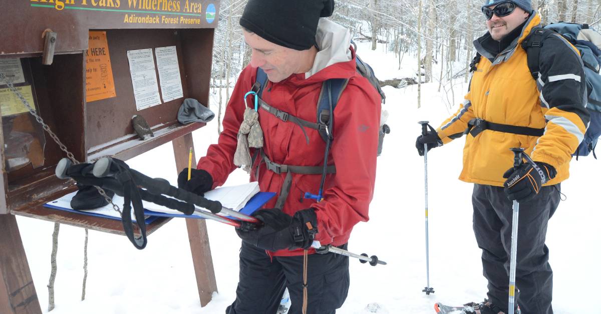 two hikers sign in at high peaks wilderness area trail register