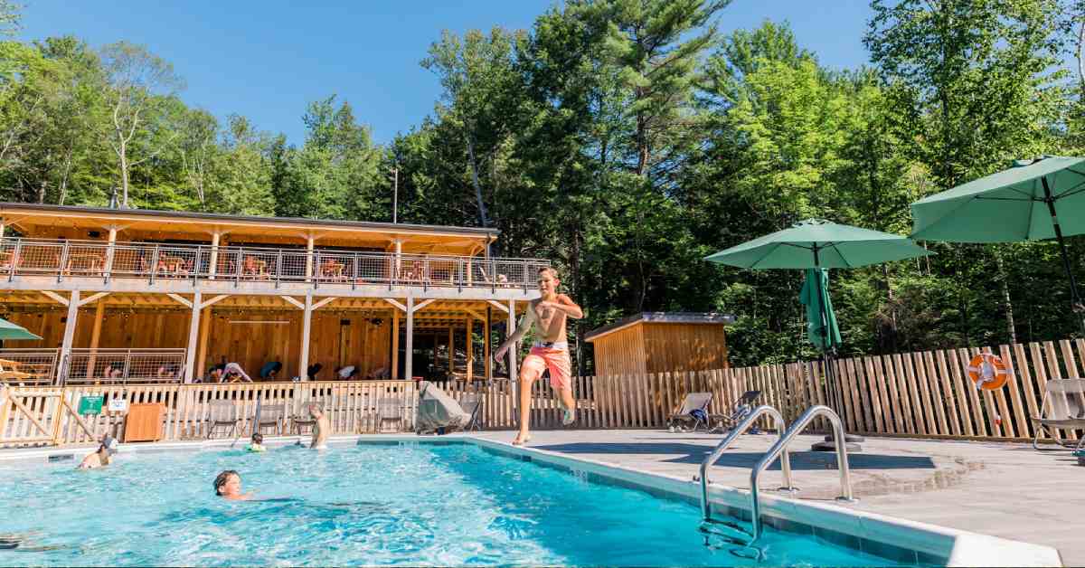 a kid jumping into an outdoor pool with a lodge nearby