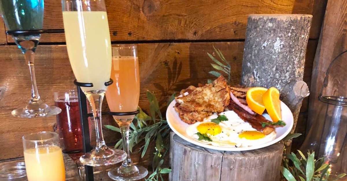 plate of brunch food of a wooden stump next to glasses of mimosas