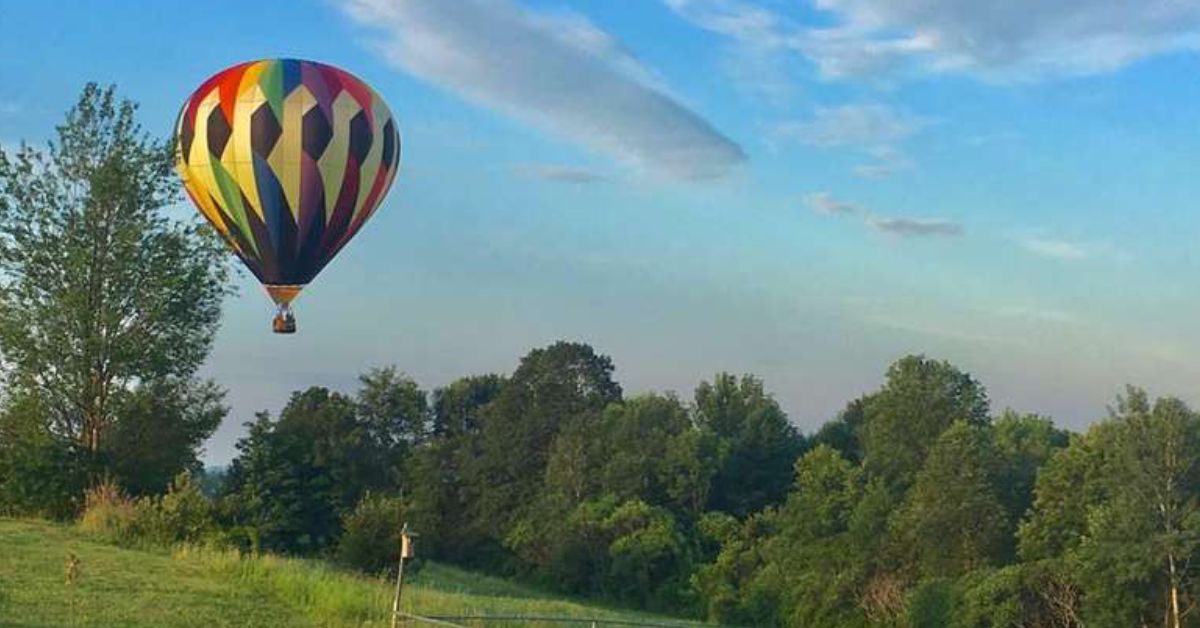 rainbow colored hot air balloon flying over a field