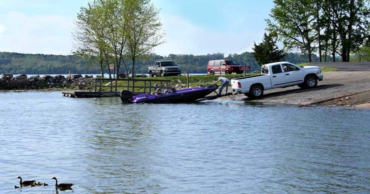 Purple boat being launched into water by a white pickup truck