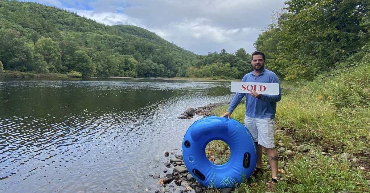 man holds a sold sign and a water tube standing by a river